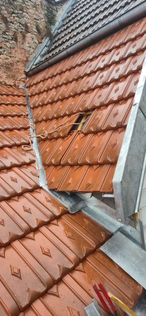 Zinguerie de noue avec tranchée à Langres Toit en tuiles orange avec des outils de chantier, vu d'en haut.