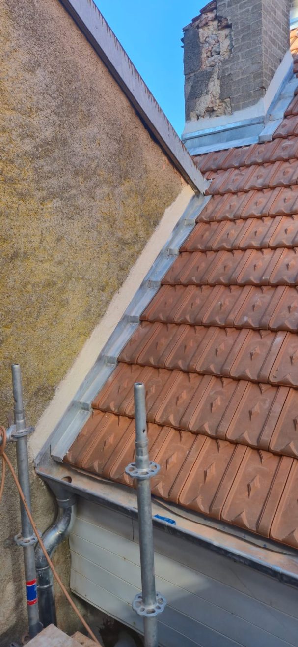 Pose de noquet avec bande à solin et solin à Langres Toit en tuiles marron avec échafaudages et mur en pierre, ciel bleu en arrière-plan.