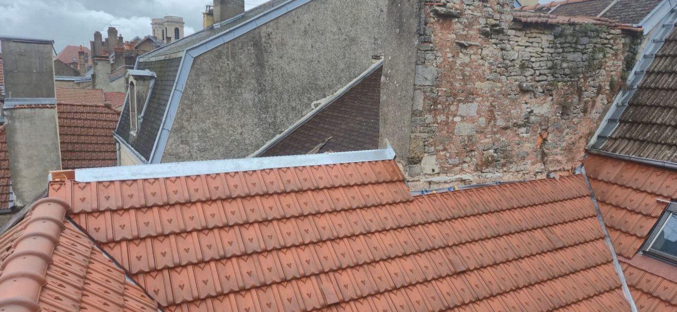Faitage en zinc à Langres Toits en tuiles, façades en pierre, ciel nuageux en arrière-plan.