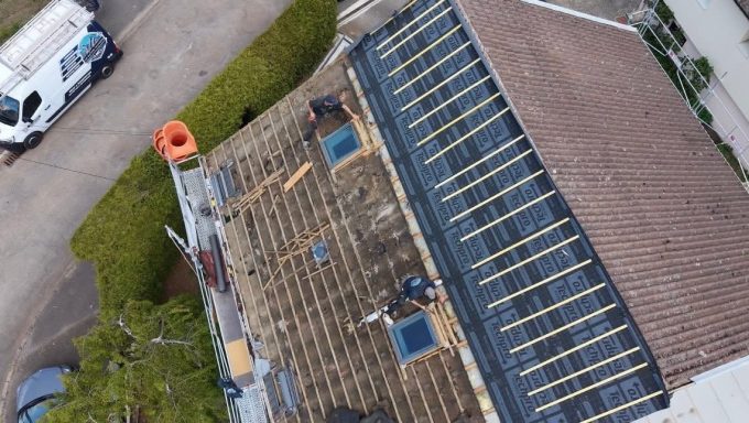 Vue aérienne d'une maison avec des travaux de toiture en cours et panneaux solaires.