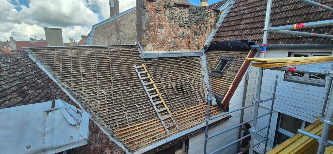 Dépose de tuiles à Langres Toit en reconstruction avec échafaudage et échelle sur un bâtiment. Ciel nuageux.
