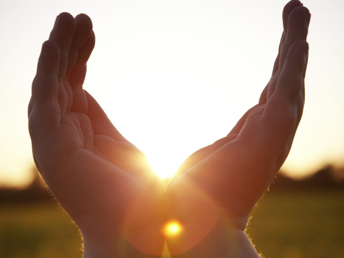 Mains ouvertes vers un soleil levant, créant une ambiance chaleureuse et lumineuse.